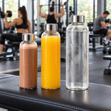 Trois bouteilles en verre avec boisson chocolatée, jus d’orange et eau sur un banc de salle de sport